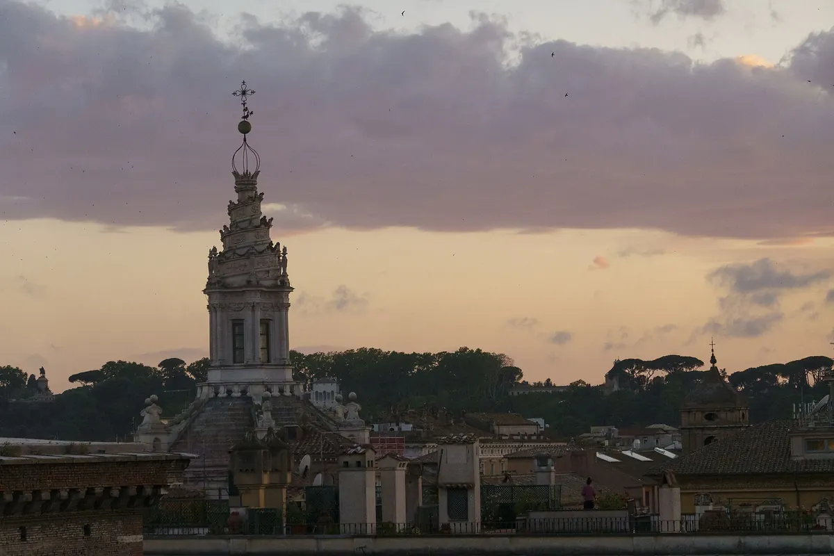 Spirálová lucerna Sant'Ivo alla Sapienza tyčící se nad římskými střechami proti růžovo-jantarové večerní obloze
